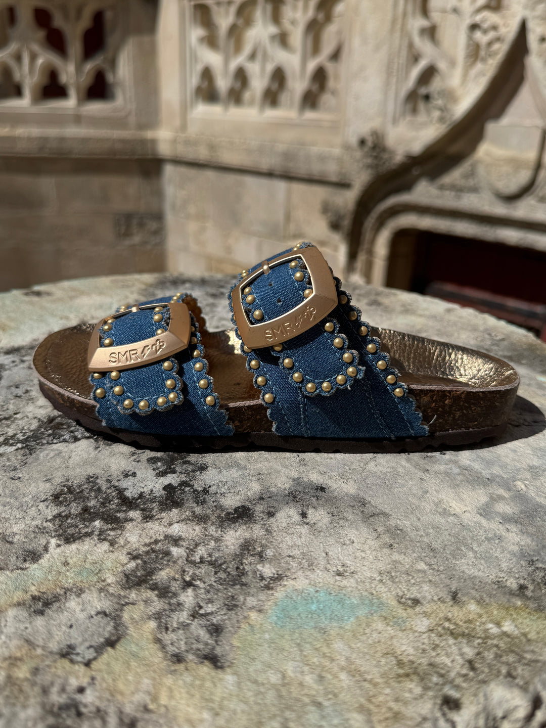 Mules en cuir bleu jeans à clous dorés avec brides réglables ARONA Semerdjian, logo SMR23 sur les boucles