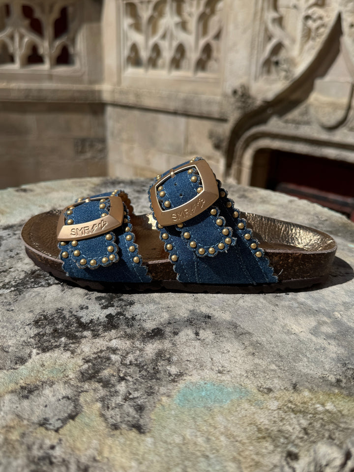 Mules en cuir bleu jeans à clous dorés avec brides réglables ARONA Semerdjian, logo SMR23 sur les boucles
