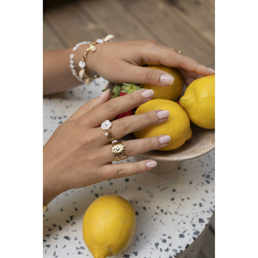 Main portant une bague dorée marguerite en acier inoxydable, réglable, hypoallergénique, résistante à l'eau et ne noircissant pas, avec des citrons en arrière-plan