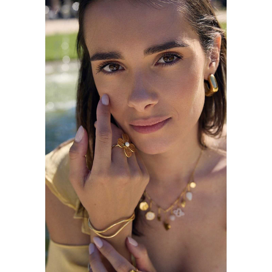 Femme portant une bague dorée fleur 4 pétales avec perle blanche, en acier inoxydable hypoallergénique