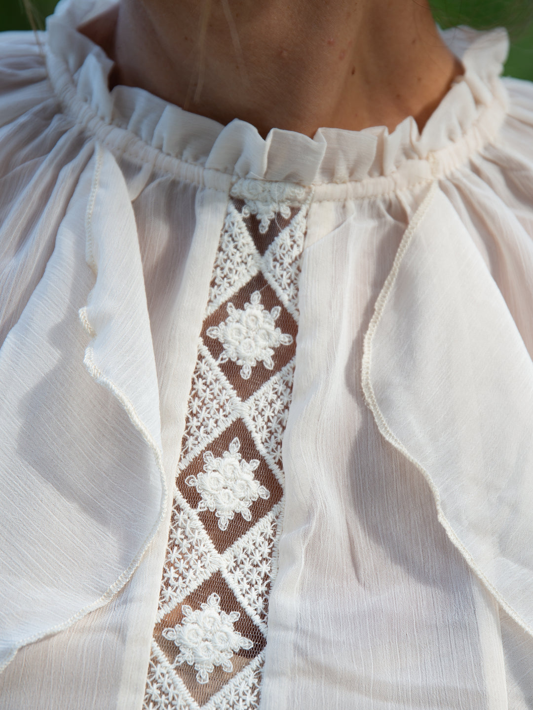 Gros plan sur le col et la broderie ajourée de la blouse écru à volants élégante