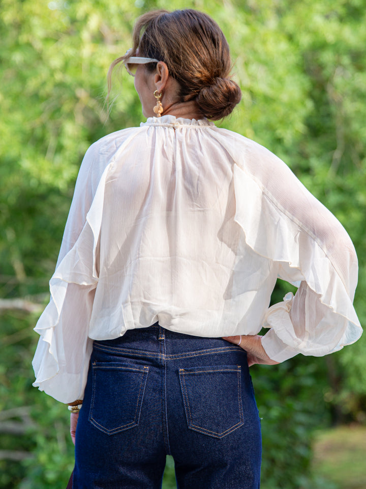Femme de dos portant une blouse écru à volants fluide avec jean brut – style bohème chic