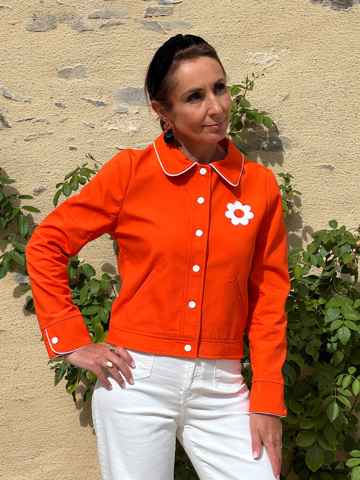 Blouson orange Miss Daisy Hippocampe pour femme avec col rétro, boutons blancs et motif fleur blanche sur la poitrine.