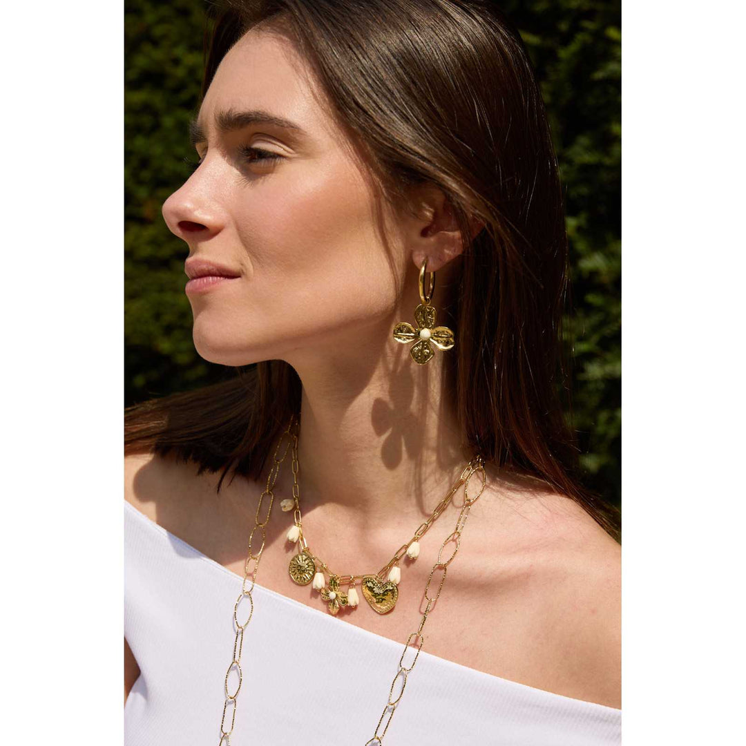 Femme portant des boucles d’oreilles dorées en acier inoxydable en forme de fleurs avec perle blanche centrale – Bijou élégant et tendance