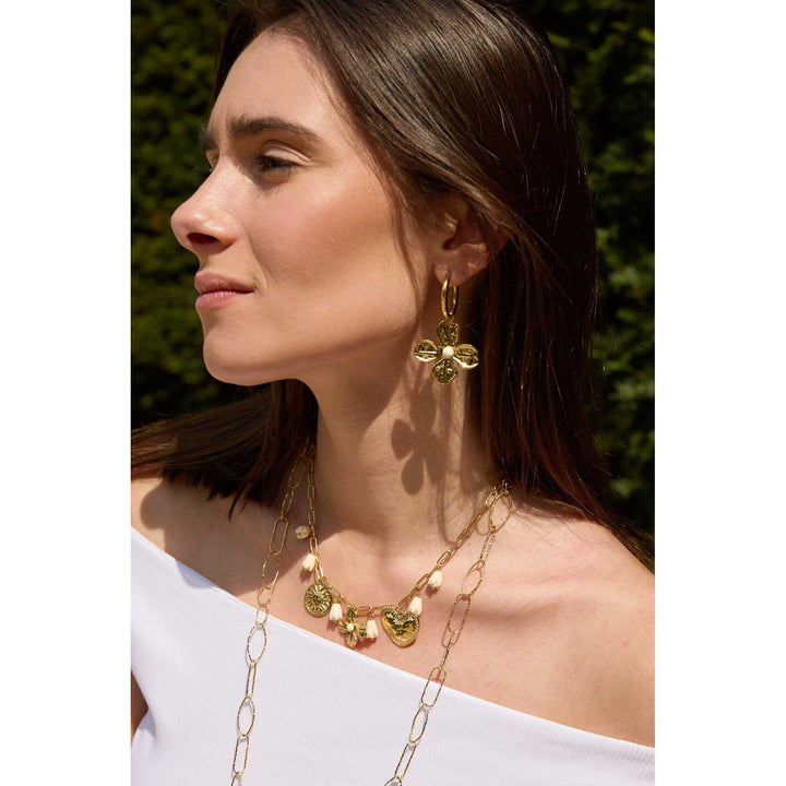 Femme portant des boucles d’oreilles dorées en acier inoxydable en forme de fleurs avec perle blanche centrale – Bijou élégant et tendance