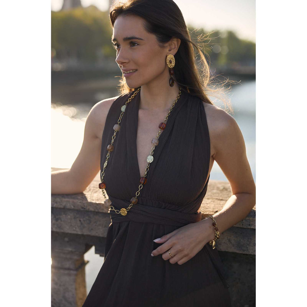 Femme portant un bracelet doré et marron en acier inoxydable avec breloques cœur, coquillage et trèfle – Bijou tendance et résistant à l’eau