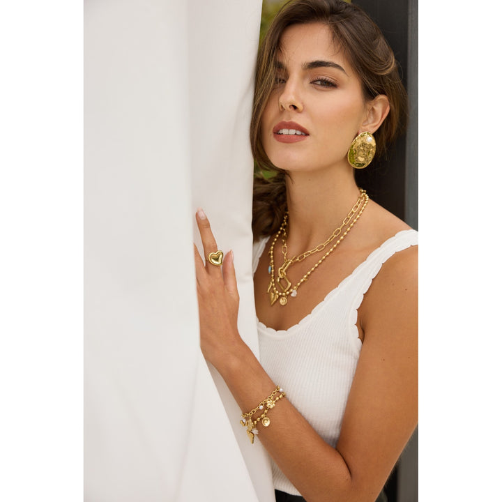 Bracelet maille doré en acier inoxydable avec mini fleurs à strass et perles blanches porté par une femme élégante