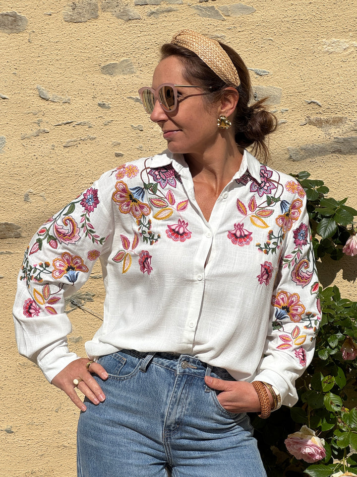 Chemisier blanc avec broderies florales multicolores, col chemise, manches longues et coupe droite fluide, élégant et confortable pour la mi-saison.