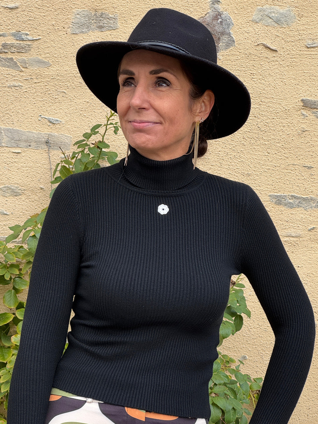 Pull col roulé noir DAISY Hippocampe pour femme, maille fine côtelée, coupe courte ajustée, manches longues et petite fleur blanche décorative sur la poitrine.