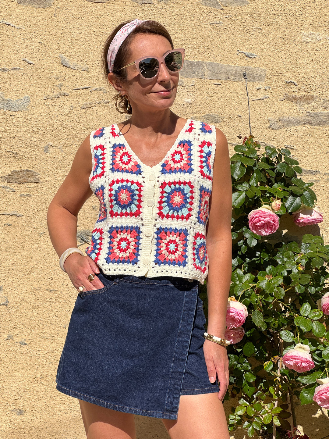 Gilet en crochet multicolore style bohème, sans manches avec col V, motifs bleu, rouge, rose et bleu ciel sur fond beige, parfait pour une tenue estivale tendance et légère.