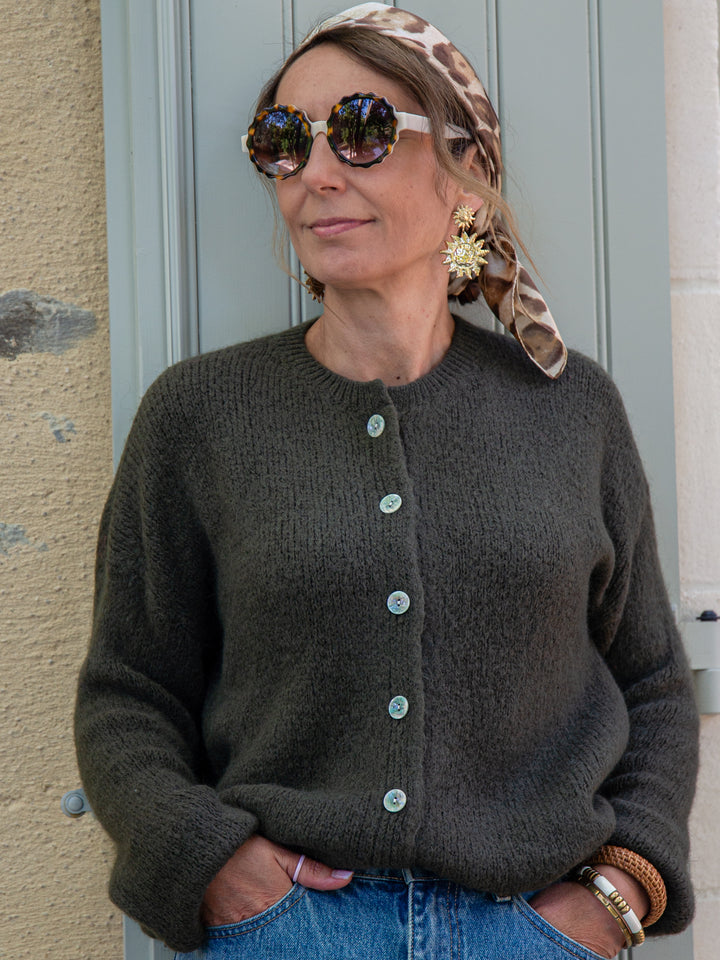 Gros plan du gilet kaki femme avec boutons nacrés, porté avec foulard imprimé et lunettes, look automne chic.