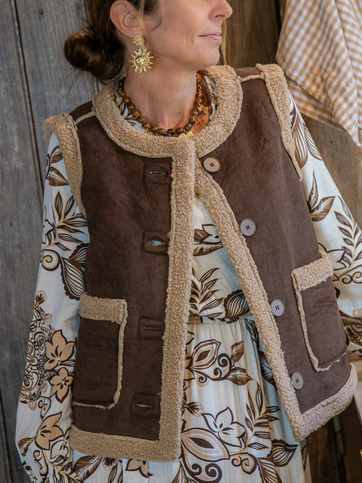 femme portant un gilet sans manches marron doublé effet mouton sur une robe fleurie bohème, look automne chic