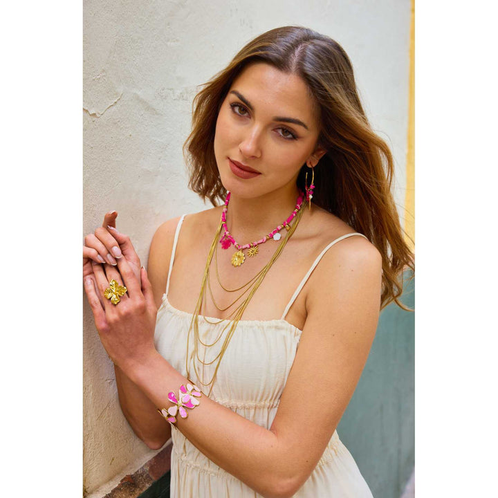 Bracelet manchette doré fleurs roses et fuchsia porté au poignet d’une femme en robe blanche, bijou en acier inoxydable hypoallergénique