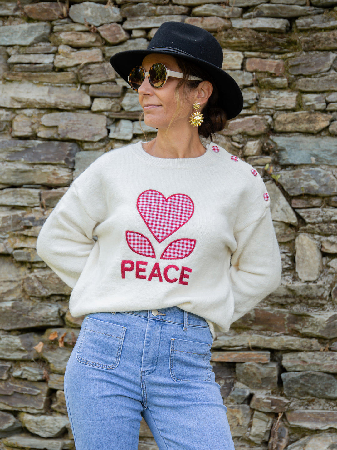 pull écru femme avec motif vichy rouge Peace porté avec jean clair et chapeau noir