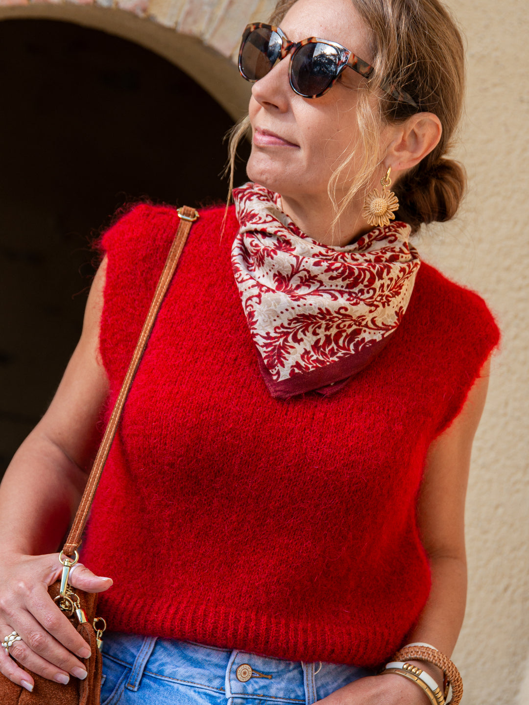 Pull sans manches rouge foncé porté par une femme avec foulard bordeaux et accessoires dorés