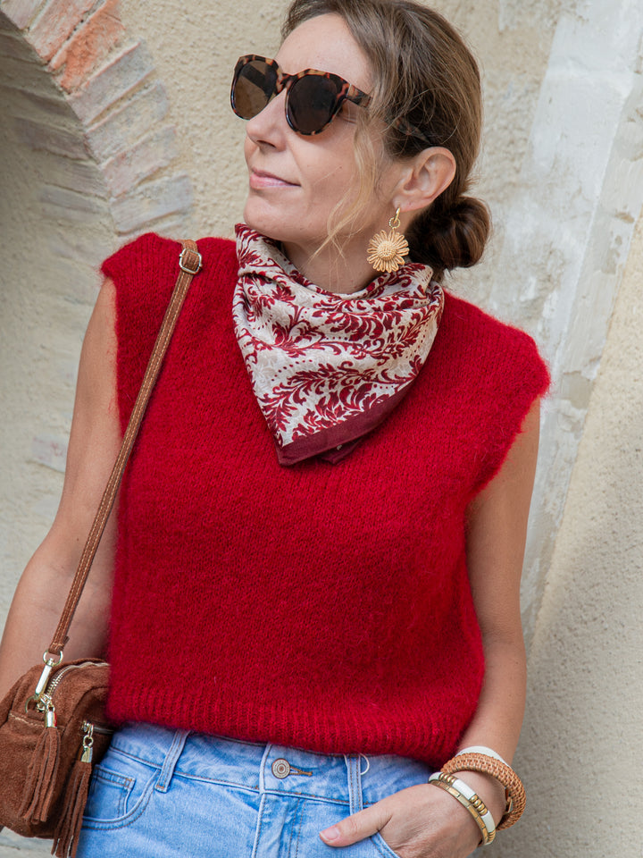Gros plan femme avec pull sans manches rouge foncé, foulard imprimé et sac en daim