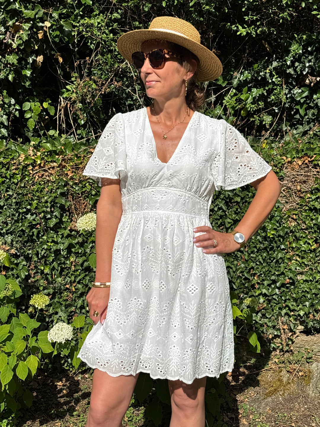Robe courte blanche en broderie ajourée, avec col V, manches courtes et coupe empire. Un modèle bohème, fluide et idéal pour l’été.