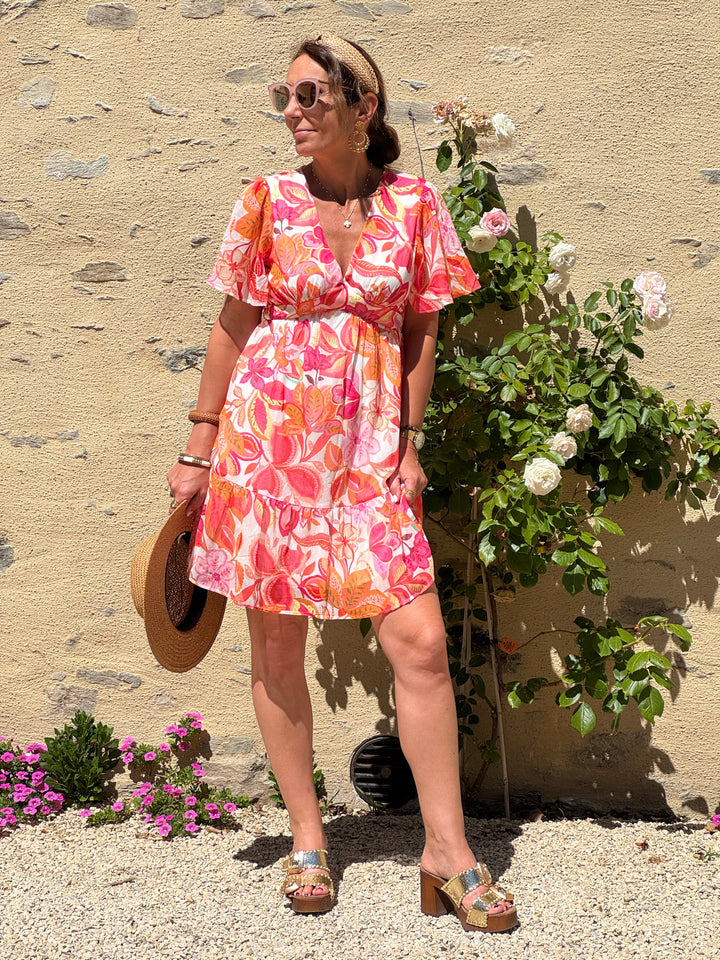 Robe courte In April 1986 à imprimé floral rose, orange, jaune et rouge sur fond blanc, coupe empire, col V et manches courtes.