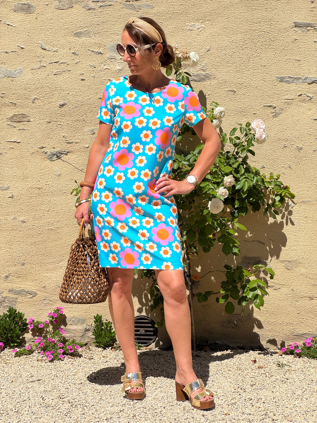 Robe courte Hippocampe à imprimé fleuri seventies écru, orange et rose sur fond bleu turquoise, avec col rond, manches courtes et coupe droite.