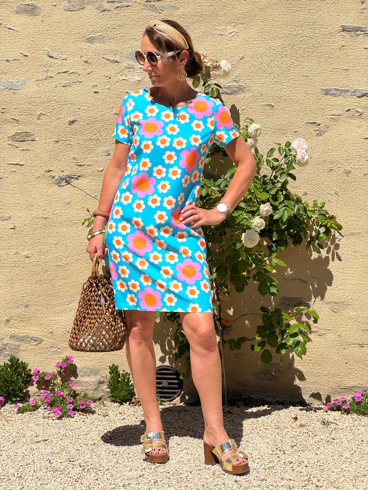 Robe courte Hippocampe à imprimé fleuri seventies écru, orange et rose sur fond bleu turquoise, avec col rond, manches courtes et coupe droite.