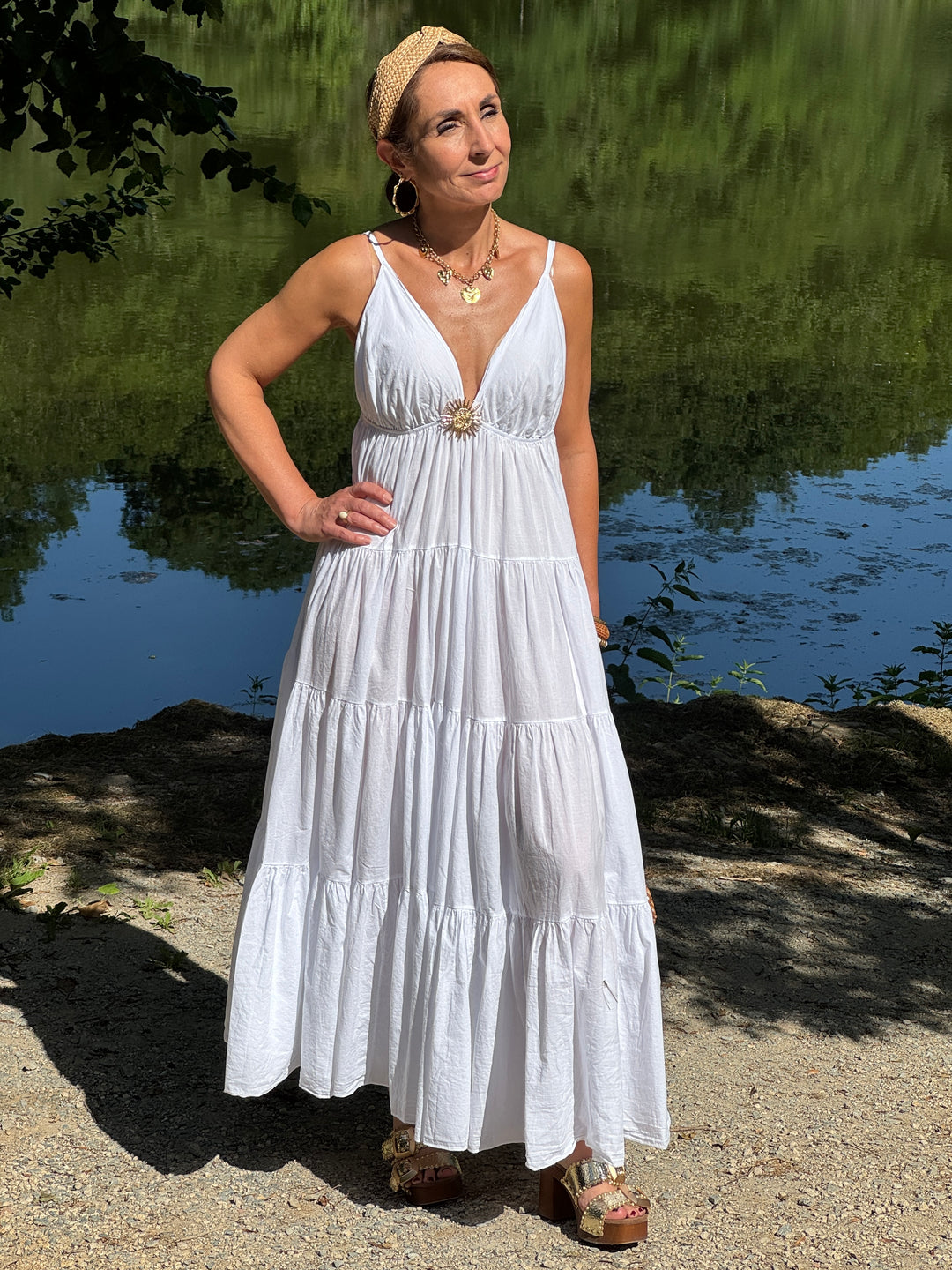 Robe longue blanche à fines bretelles réglables avec décolleté V, bijou soleil doré  et coupe empire fluide, légère idéal pour l’été.