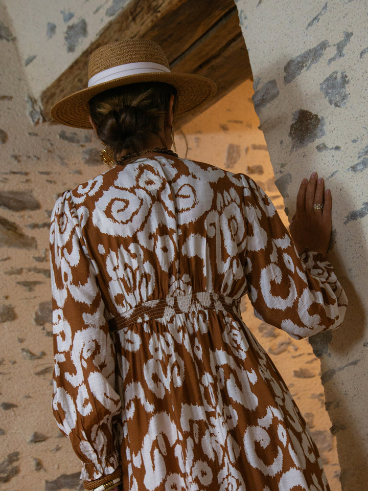 vue de dos d’une femme en robe longue bohème marron et blanc avec chapeau en paille, look automne chic