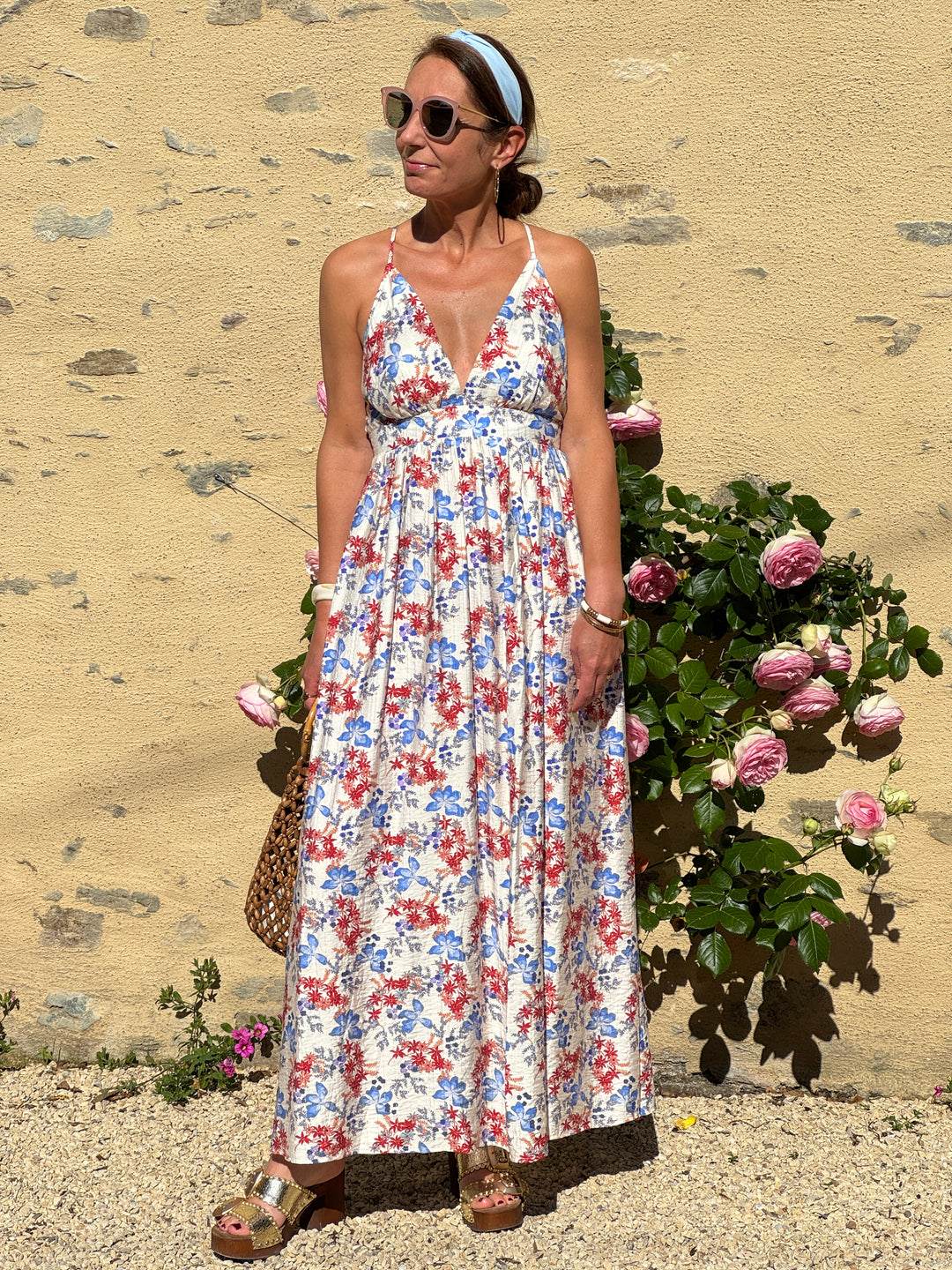 Robe longue fluide à imprimé floral rouge et bleu sur fond beige avec liseré doré, fines bretelles réglables et coupe empire, idéale pour l’été