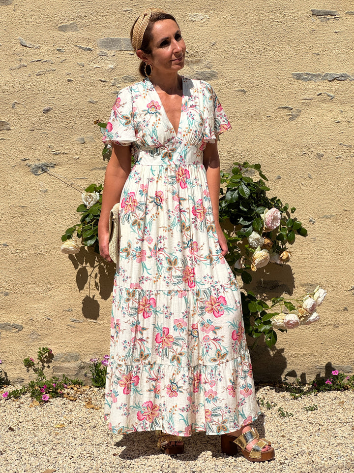 Robe longue fluide à imprimé floral multicolore sur fond blanc, avec col V, coupe empire et manches courtes volantées. Une robe légère et élégante idéale pour l’été.