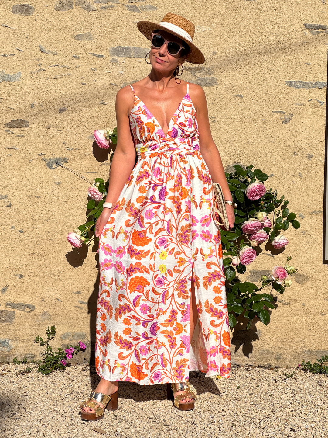 Robe longue à imprimé floral orange, rose et jaune sur fond beige, avec fines bretelles réglables, col V, coupe empire fluide et fente sur le bas, parfaite pour l’été.
