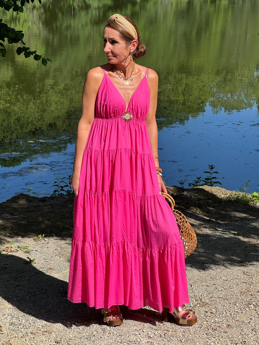 Robe longue fuchsia à fines bretelles réglables avec décolleté en V, coupe empire et bijou soleil doré. Une robe fluide, légère et élégante, parfaite pour l’été.