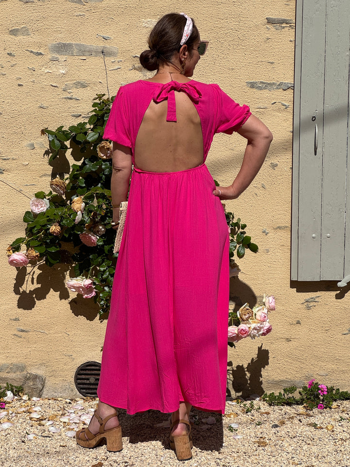 Robe longue fuchsia fluide et légère avec col V, manches courtes élastiquées, dos ouvert avec nœud et coupe ample élégante, idéale pour un look d’été.