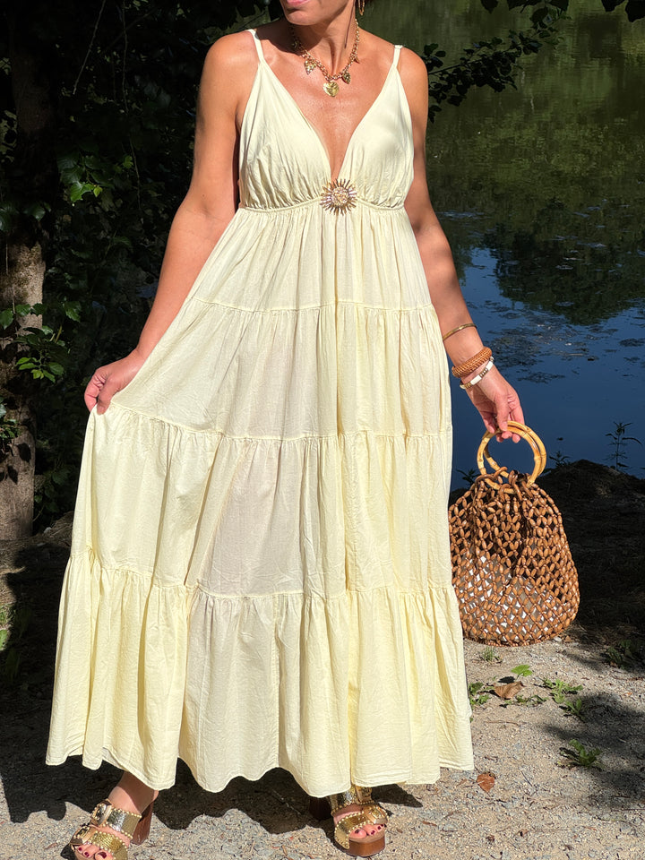 Robe longue jaune à fines bretelles réglables, décolleté V et bijou soleil doré. Sa coupe empire fluide et légère en fait une pièce élégante et idéale pour l’été.