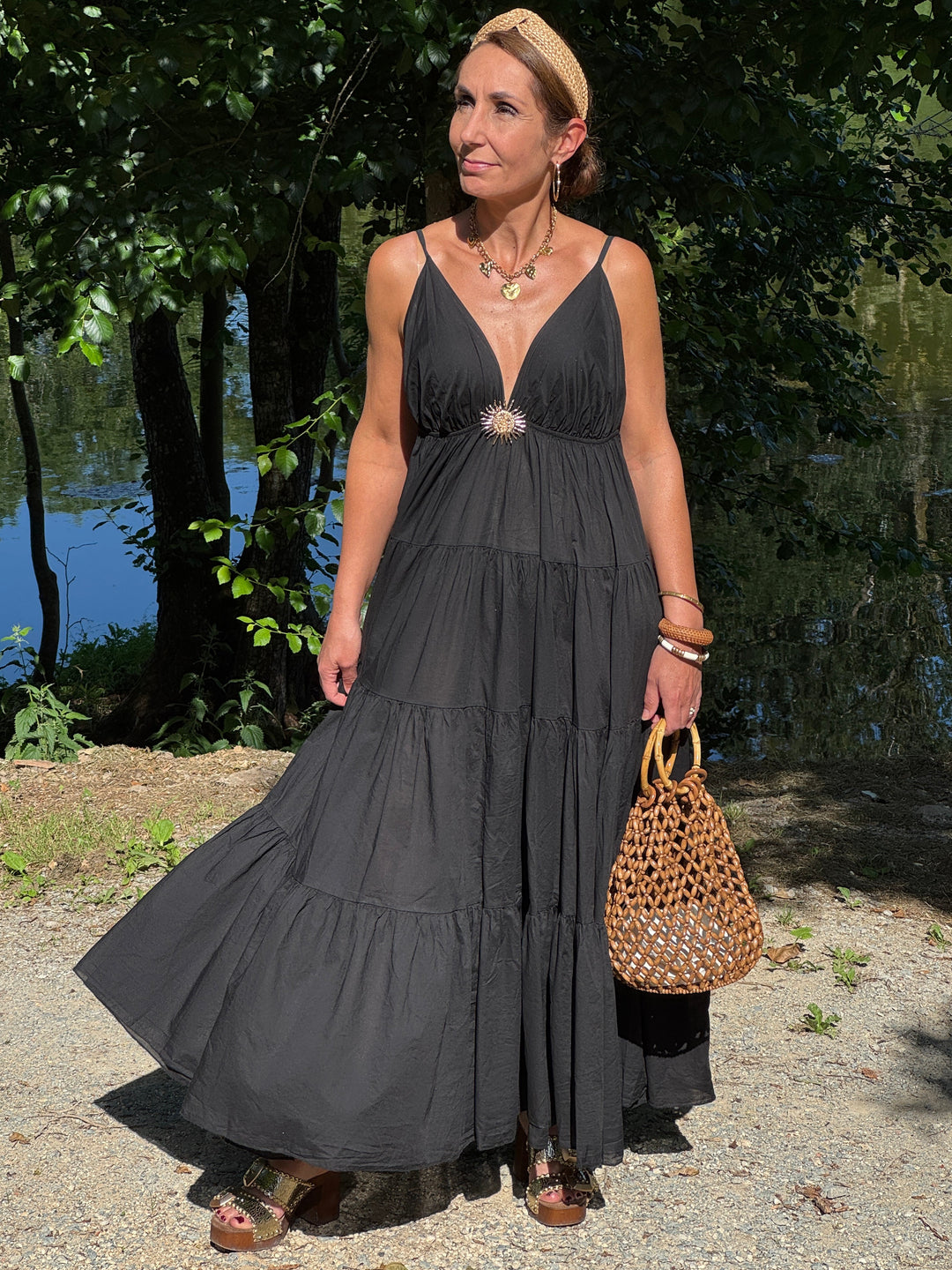 Robe longue noire à fines bretelles réglables avec décolleté V, bijou soleil doré et coupe empire fluide, légère et élégante pour l’été.