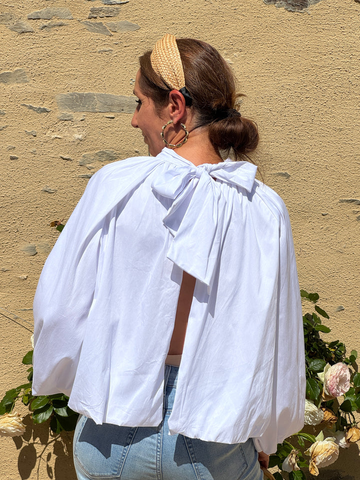 Top blanc fluide à manches longues avec dos ouvert et grand nœud dans le haut du dos. Une blouse moderne et élégante à la coupe blousante.
