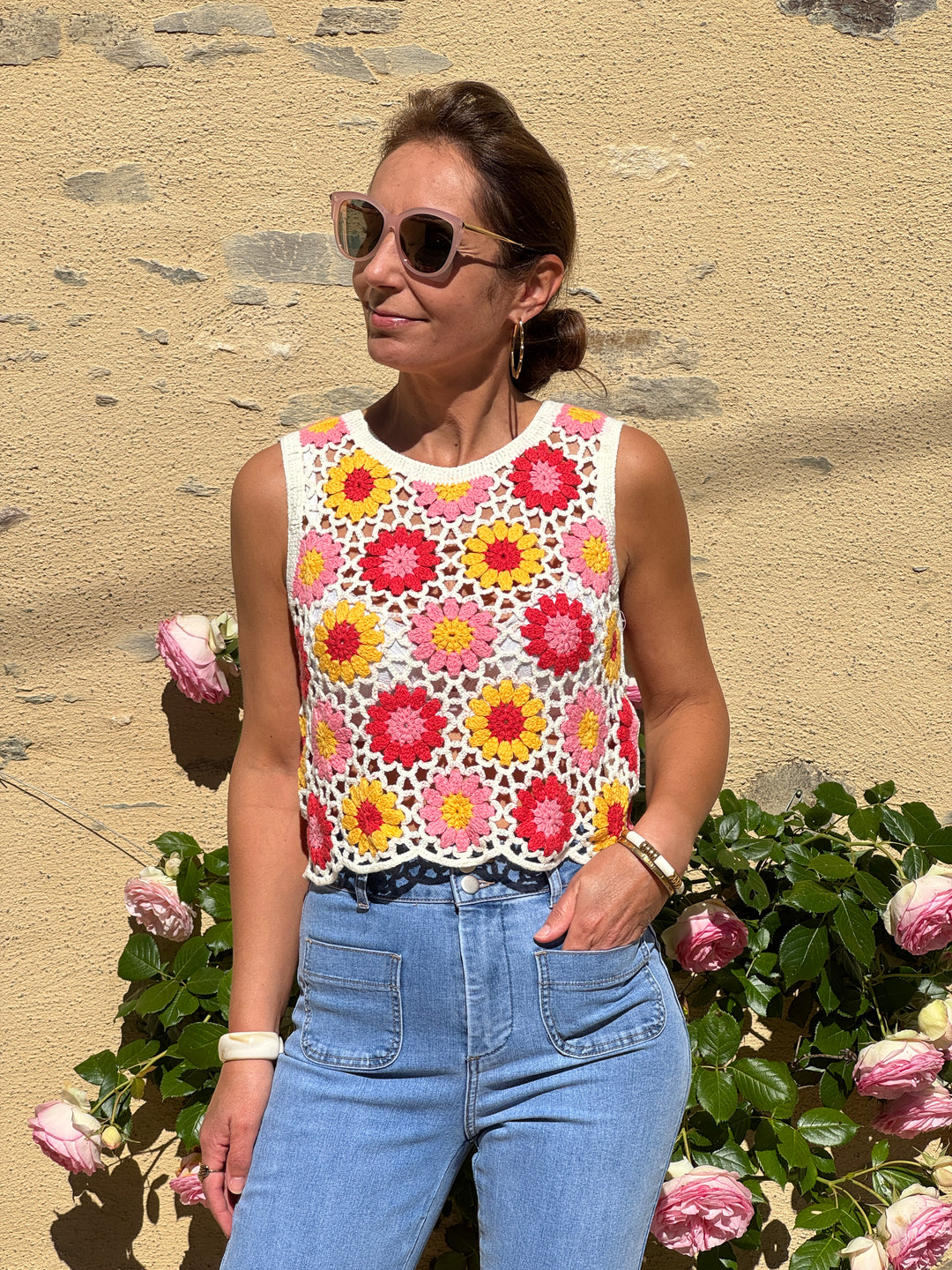 Top en crochet ajouré multicolore avec fleurs jaunes, rouges et roses sur fond blanc, col rond et coupe légère, parfait pour l'été.