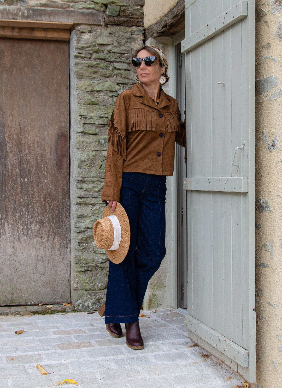 femme portant une veste à franges marron en suédine avec jean brut et chapeau, look bohème chic